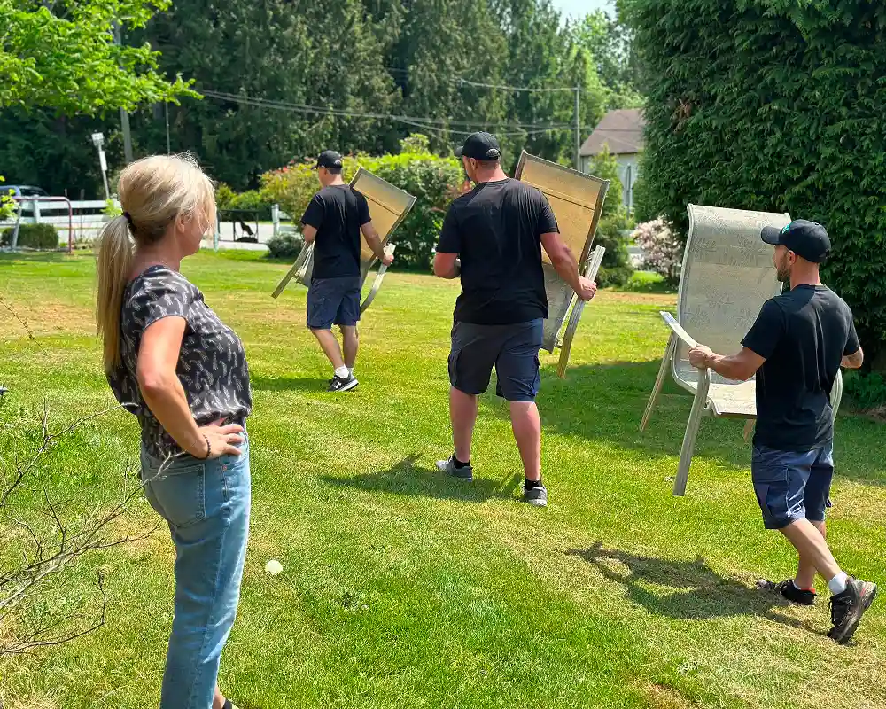 Big Phil's Rubbish Removal crew carrying patio chairs across a lawn during a cleanout
